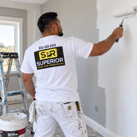 A professional painter wearing a Superior Paint & Remodeling company shirt using a roller to apply fresh paint to an interior wall in Kansas City.